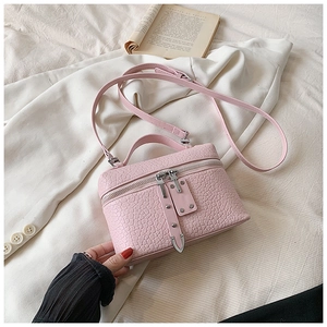 Detail of pink croc-textured crossbody bag with silver zippers on white fabric