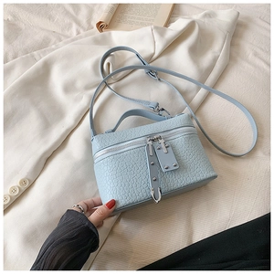 Detail of light blue crocodile embossed leather square bag on cream blazer background
