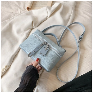 Detail of light blue crocodile pattern square handbag with double zippers and strap