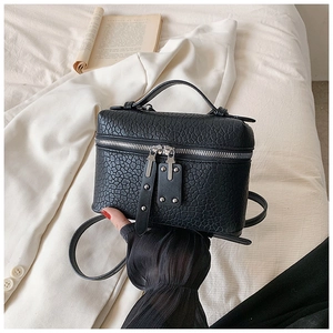 Close-up of black textured leather mini box bag with dual zippers and silver rivets