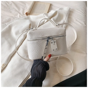 Detail of white crocodile texture leather handbag with silver zipper on white blazer