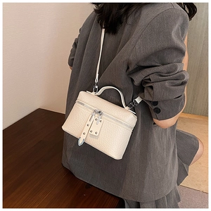 Detail of a cream faux ostrich skin crossbody bag showing texture and rivet strap