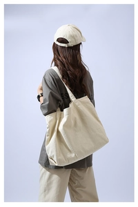 Rear view of a model wearing a large cream canvas tote bag with wide shoulder straps