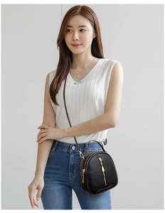 Close-up of black lychee grain leather mini bucket bag with gold zippers worn by a model