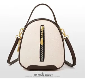 Detail of beige lychee leather crossbody bag with brown trim and gold vertical zipper