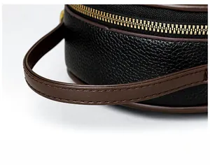 Macro detail of black litchi grain leather bag with brown handle and gold metal zipper