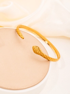 Detail of gold snake-head open cuff with textured scale pattern on cream silk background