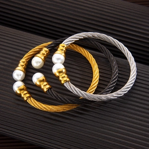 Detailed view of woven cable open bangles in gold, silver, and black with faux pearls
