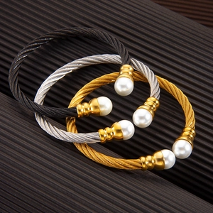 Three twisted wire cuff bracelets in black silver and gold with pearl ends on brown surface