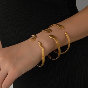 Three-piece gold snake-shaped open bracelets with engraved scales on a model's arm