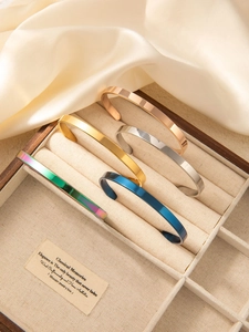 Detailed close-up of five minimalist C-shape bracelets in assorted finishes on silk