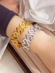 Detailed close-up of hollow heart-shaped bangles in polished gold and silver finishes