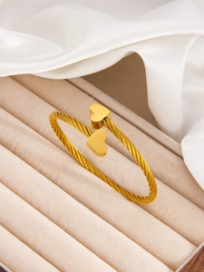 Detail of twisted wire golden heart bangle displayed on elegant silk and jewelry box