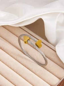 Detail of silver twisted cable bracelet with golden heart tips on beige velvet