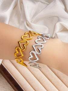 Close-up of hollow heart bangles in gold and silver finish worn on a wrist
