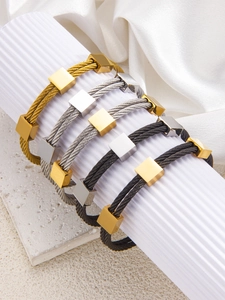Detalle de brazaletes ajustables de cable de acero trenzado en oro, plata y negro