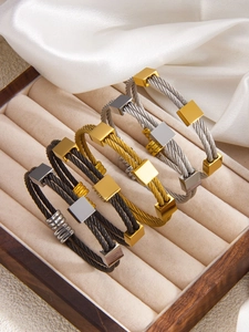 Primer plano de cuatro pulseras de cable de lujo en oro y plata sobre terciopelo beige