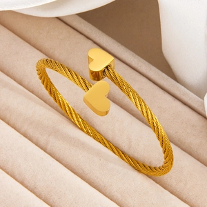 Minimalist 18k gold plated twisted heart bangle on a soft beige velvet jewelry display