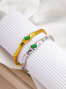 Macro detail of wave-textured 18k gold and silver bangles with green emerald stones