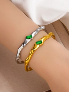 Detail of irregular lava texture gold and silver bangles with emerald-cut green gemstones