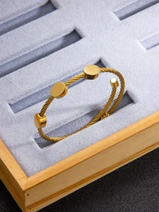 Detail of twisted cable cuff bracelet with three polished gold discs in a jewelry box
