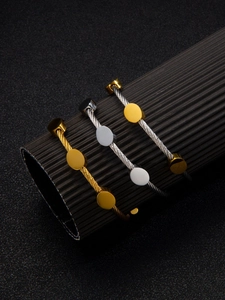 Detail view of twisted gold and silver cable bracelets on a textured black stand