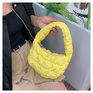 Detail of yellow quilted cloud bag with metal chain strap held by a model