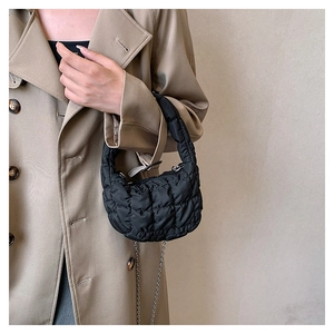 Close-up of black quilted cloud bag texture and metal chain strap on beige trench coat