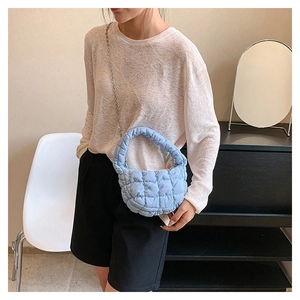 Blue quilted crescent bag with chain strap held by model in minimalist indoor setting
