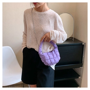 Detail of purple quilted puffer bag with silver chain strap worn by a female model