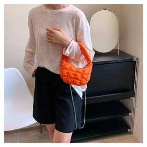 Detailed view of orange quilted cloud bag with metallic silver chain strap on model