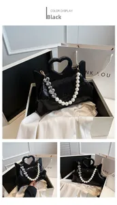 Detail van zwarte handtas met pailletten, hartvormig handvat en parel-hartketting