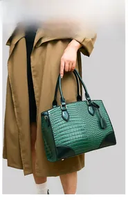 Détail d'un sac à main vert foncé à motif crocodile porté par un mannequin en trench-coat