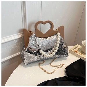 Detail van zilveren pailletten tas met hartvormig handvat en parelketting op tafel