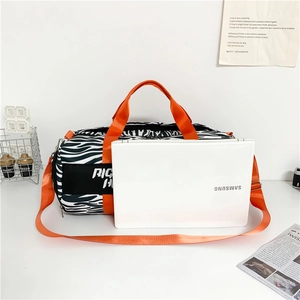 Zebra print travel bag with orange straps next to a laptop for size comparison