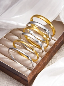 Polished gold and silver stainless steel bangles set displayed on wooden jewelry box