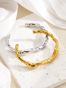 Detailed view of textured C-shape bangles in gold and silver on a white stone background