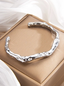 Detailed macro view of silver C-shaped cuff bracelet with irregular molten lava texture
