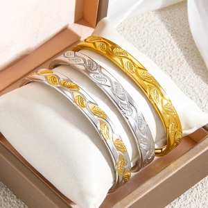 Detail of three leaf-patterned bracelets in gold and silver finish inside a gift box