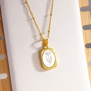 Collana con ciondolo floreale rettangolare dorato con catena a sfere su pelle bianca