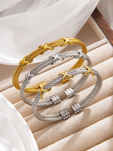 Three twisted cable cuff bracelets in gold, silver, and two-tone finishes on velvet