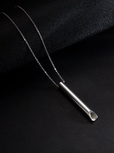 Macro d'un pendentif sifflet de méditation argenté sur cuir noir avec lumière vive