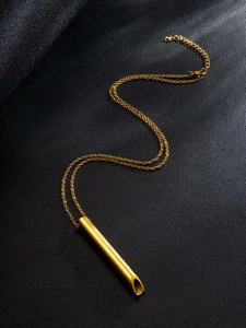 Détail macro du pendentif sifflet de méditation plaqué or 18k sur fond de cuir noir