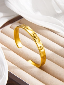 Detail of gold-plated open bangle with hammered texture and three star motifs on velvet