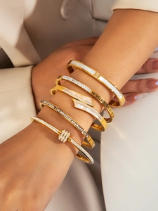 Close-up of gold-plated bangles set with white shell and roman numeral details on wrist