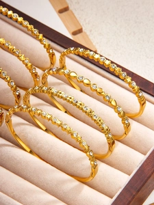 Detailansicht von goldenen Kleeblatt-Armreifen mit Strasssteinen in einer Schmuckschatulle