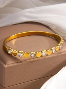 Detailed close-up of gold heart bangle with zircon stones on a brown jewelry box