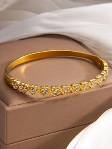 Close-up of gold heart bracelet featuring link chain set with white crystals on a stand