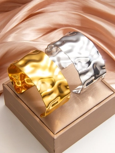 Detail of 18k gold and silver plated textured metal cuffs on luxury satin background