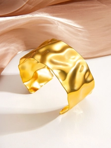Macro view of wide gold-plated cuff bracelet featuring a unique hammered wave texture